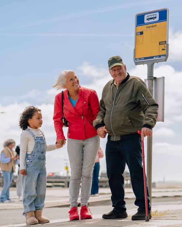 Opa en oma staan met kleinkind bij bushalte